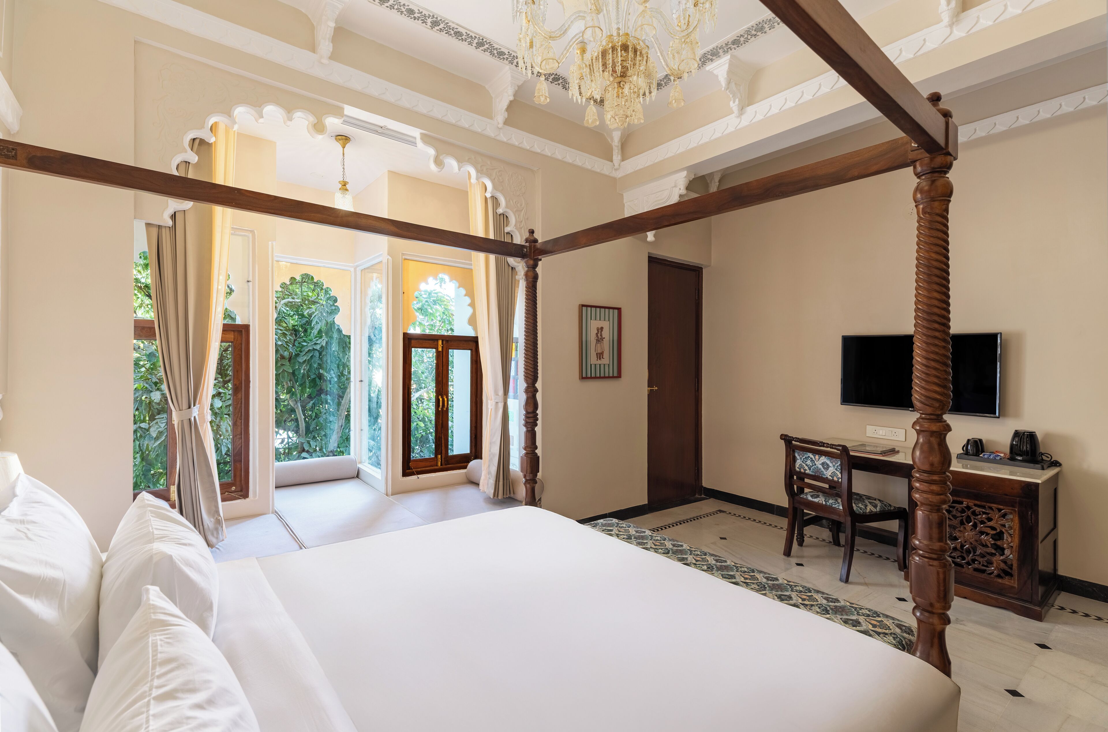 A four-poster bed in a room with a desk, chair, and television.