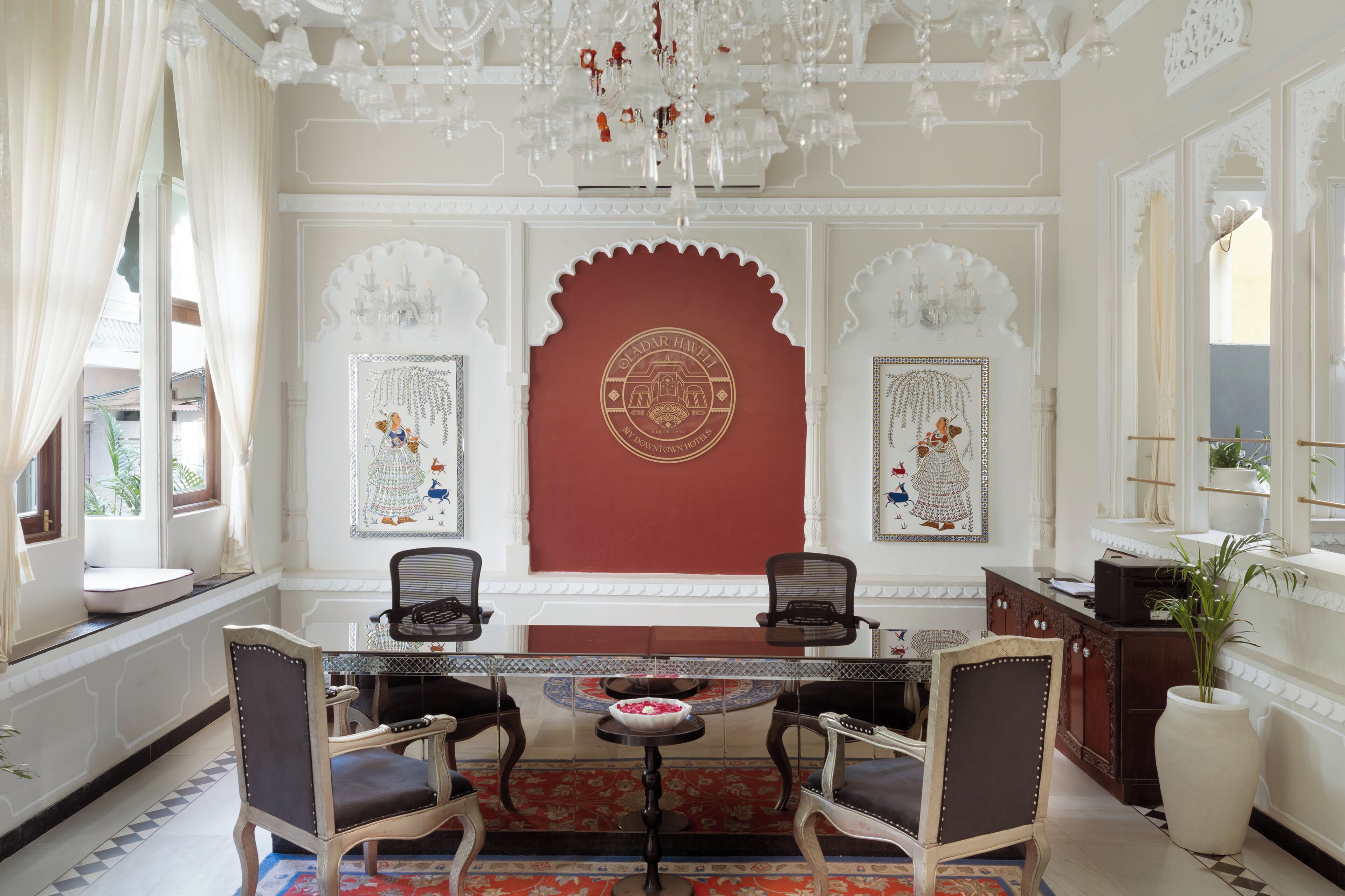 Une chambre d’hôtel de style traditionnel indien, avec un mur d’accent rouge, des lustres et un décor riche et élaboré.