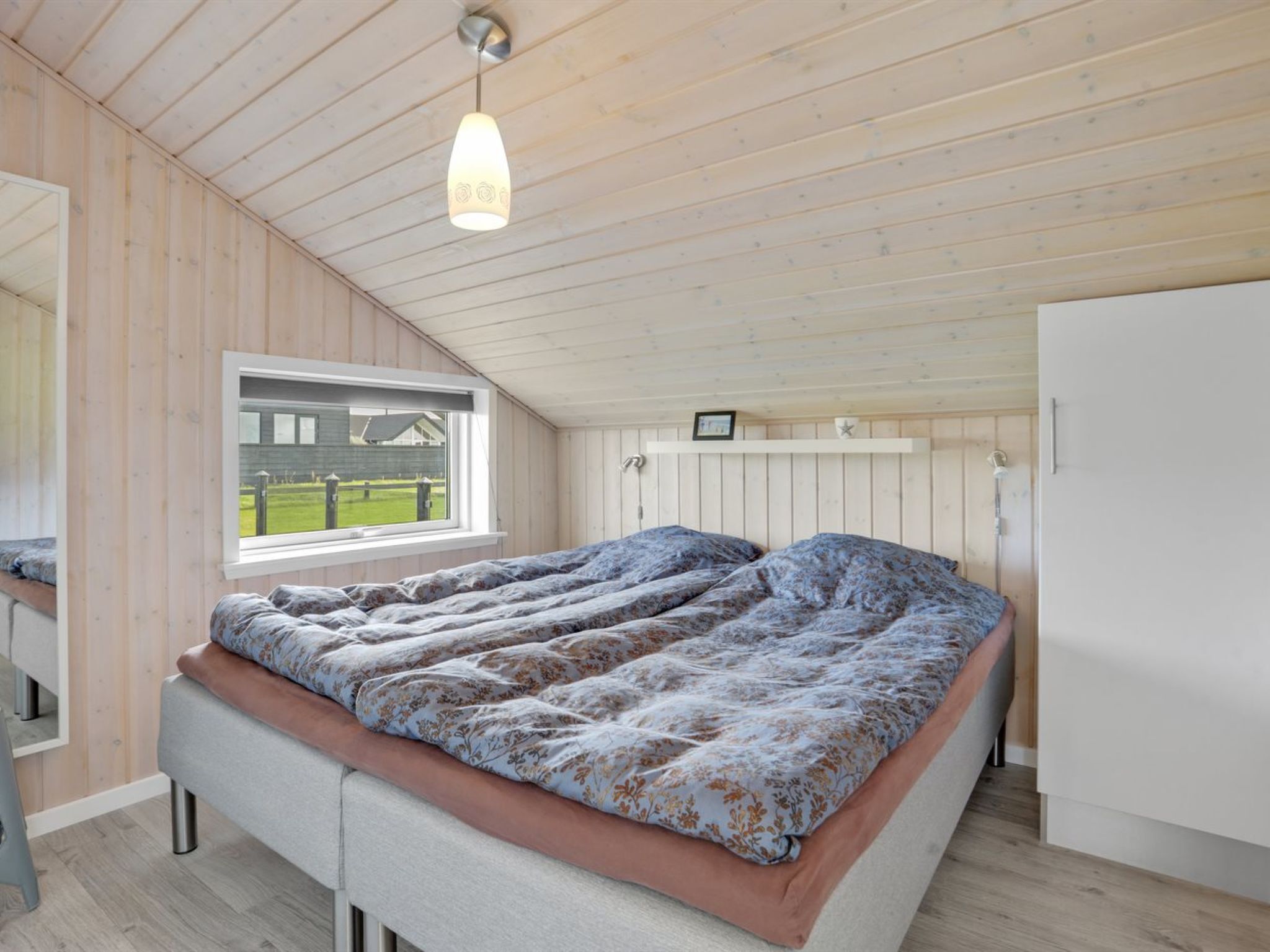 Une chambre à coucher avec un lit, une fenêtre, un luminaire au plafond et une armoire blanche.