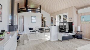 Tilava olohuone, jossa on korkea katto, ruokailutila pöytineen ja tuoleineen sekä modernisti varusteltu keittiö.