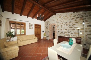 Ein Wohnzimmer mit einer Couch, einem Esstisch mit Stühlen, einer Chandelüster und einer Steinwand.
