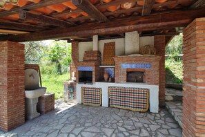 Cocina exterior con horno de ladrillo, piso de piedra y techo rústico de madera.