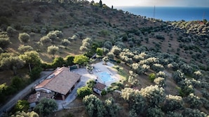 An aerial view of a property with a swimming pool, a house with a tiled roof, and a hilly landscape with sparse vegetation. - VVilla Cosentino is an enchanting retreat immersed in the Mediterranean nature of Sicily, where peace, privacy and authenticity come together. Surrounded by centuries-old olive trees, fruit trees and breathtaking sea views, this villa is the ideal place  (Acquedolci)