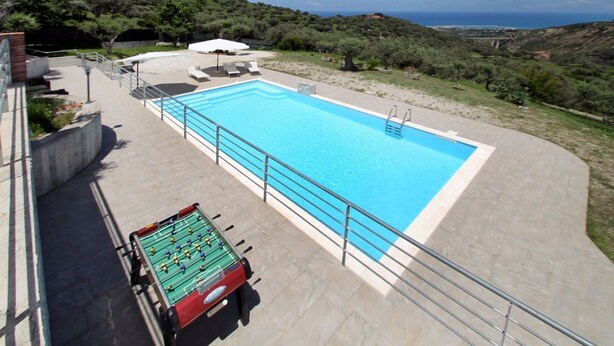 A rectangular pool with a metal railing, a foosball table, and lounge chairs. - VVilla Cosentino is an enchanting retreat immersed in the Mediterranean nature of Sicily, where peace, privacy and authenticity come together. Surrounded by centuries-old olive trees, fruit trees and breathtaking sea views, this villa is the ideal place  (Acquedolci)