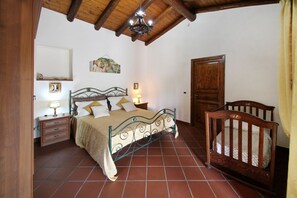 A bedroom with a bed, bedside tables, a crib, a wooden door, and a ceiling with exposed beams. - VVilla Cosentino is an enchanting retreat immersed in the Mediterranean nature of Sicily, where peace, privacy and authenticity come together. Surrounded by centuries-old olive trees, fruit trees and breathtaking sea views, this villa is the ideal place  (Acquedolci)