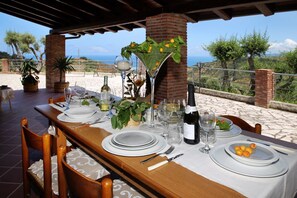 A table set for a meal with a view of the sea, a bottle of wine, and a martini glass. - VVilla Cosentino is an enchanting retreat immersed in the Mediterranean nature of Sicily, where peace, privacy and authenticity come together. Surrounded by centuries-old olive trees, fruit trees and breathtaking sea views, this villa is the ideal place  (Acquedolci)