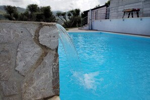 A swimming pool with a stone structure on the left and a modern building in the background. - VVilla Cosentino is an enchanting retreat immersed in the Mediterranean nature of Sicily, where peace, privacy and authenticity come together. Surrounded by centuries-old olive trees, fruit trees and breathtaking sea views, this villa is the ideal place  (Acquedolci)