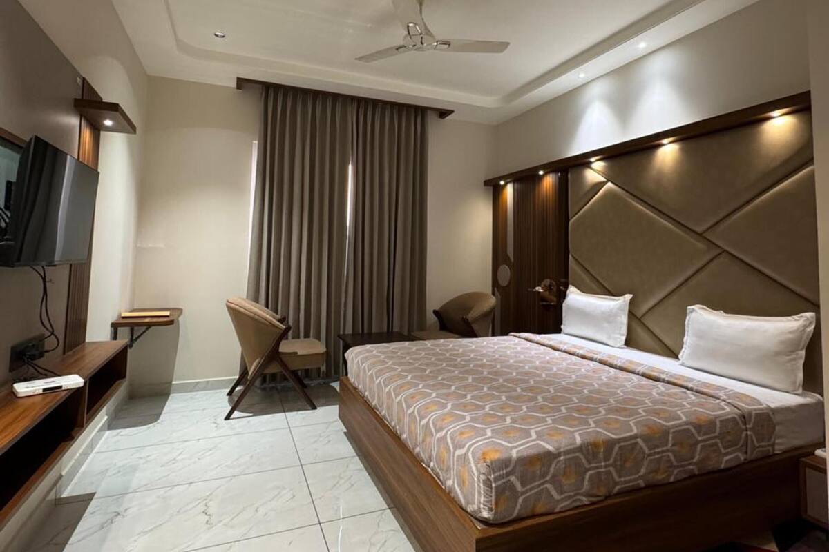 A hotel room with a bed, a desk, a chair, a TV, and a ceiling fan.