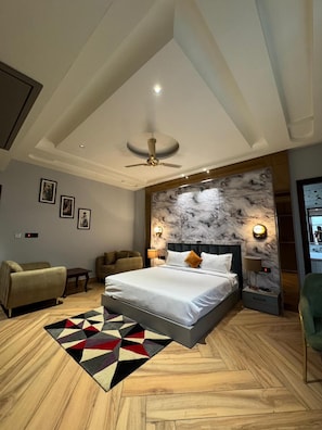 A modern bedroom with a large bed, a ceiling fan, marble wall, and a geometric rug.