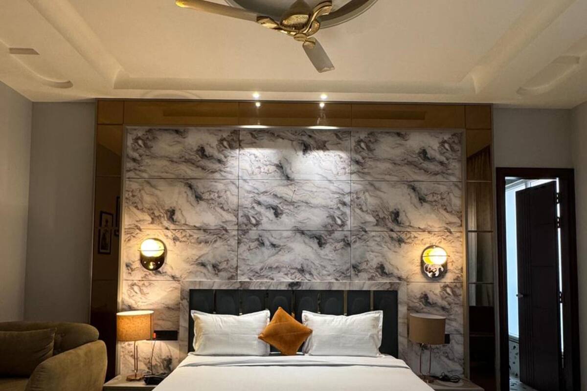 A modern bedroom with a large bed, marble headboard, two bedside lamps, and a ceiling fan.