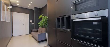 A modern kitchen with built-in ovens, a sofa, and a potted plant.