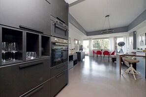 A modern kitchen with stainless steel appliances, a dining area with red chairs, and large windows. - Exclusive apartment on the Circus Maximus (Roma)