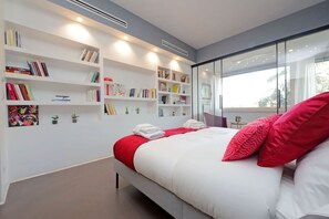 A modern bedroom with a large bed, white and red bedding, and built-in bookshelves filled with books and decorative items. - Exclusive apartment on the Circus Maximus (Roma)