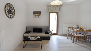A living room with a sofa, a coffee table, a dining table with chairs, a clock, and a window with curtains. - Peaceful Flat Surrounded by Nature (Umag)