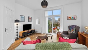 En moderne stue med et fladskærms-tv, trægulv, en sofa, et sofabord og udsigt ud gennem en stor skydedør.