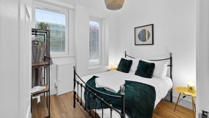 Et soveværelse med seng, sengebord, hængende lampe og et vindue med persienner.