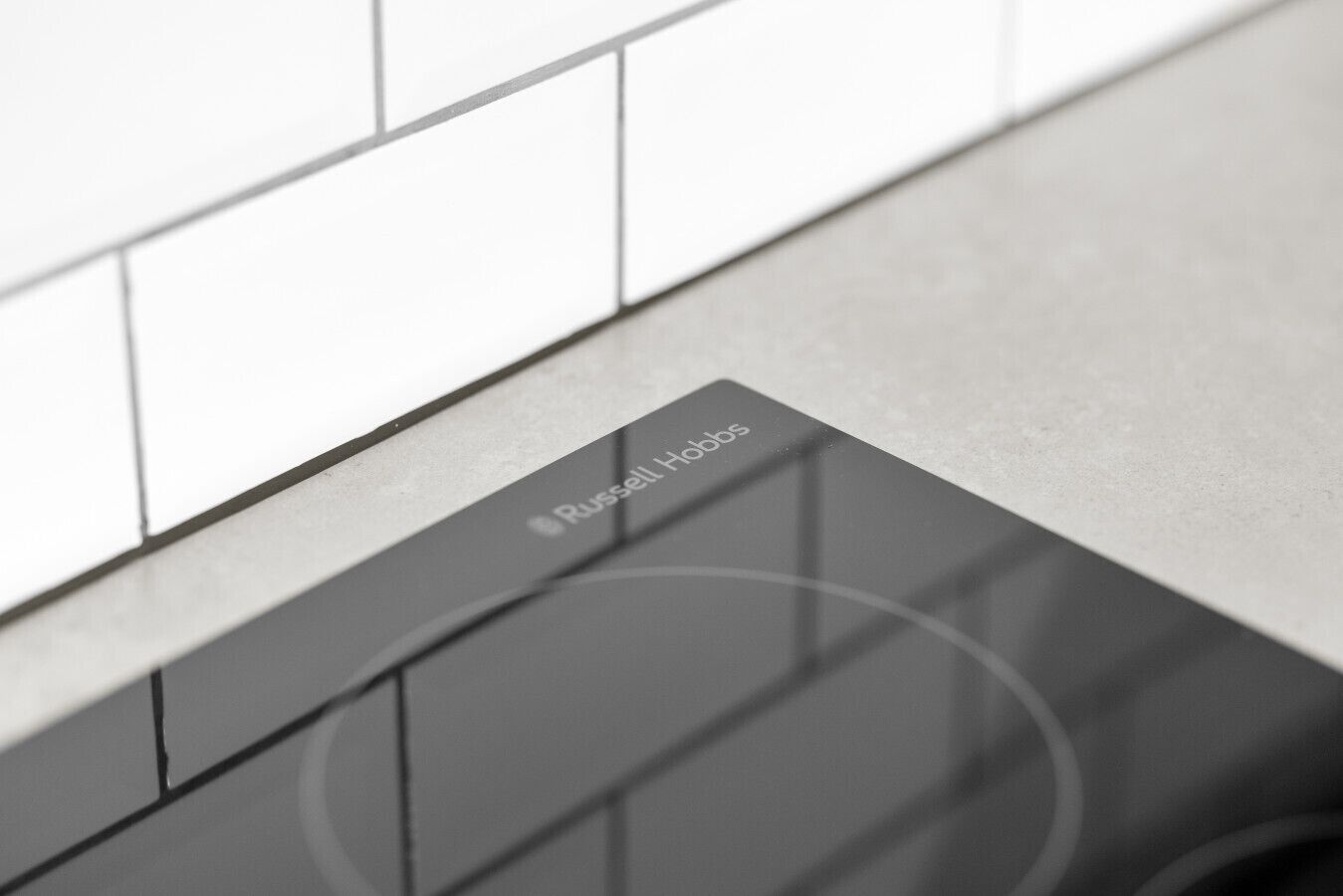 A modern kitchen with white tiles and a sleek, dark countertop.