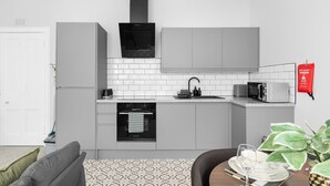 Une cuisine moderne avec des meubles gris, une hotte noire, un four encastré, un four à micro-ondes et un évier. Un panneau rouge indiquant les consignes de sécurité incendie est affiché sur le mur.