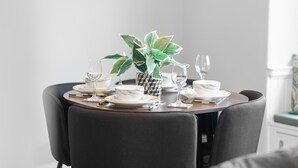 Une table à manger dressée avec de l’assiette blanche, des bols et des verres à vin, entourée de chaises sombres.