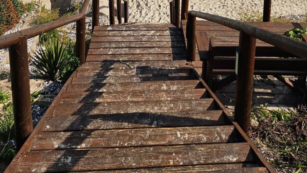 A wooden staircase leading to a beach with large rocks and a clear view of the ocean.