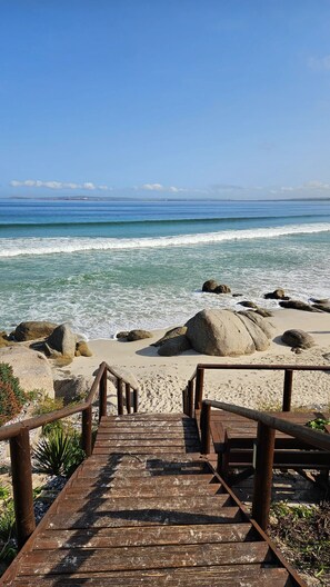 A wooden staircase leading to a beach with large rocks and a clear view of the ocean. - Langebaan Villa Retreat | 1 min Walk to Private Beach | Exclusive Estate (Langebaan)