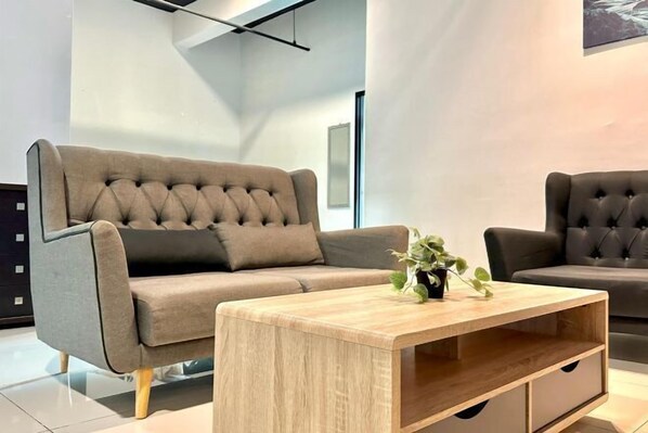 A modern living room with a grey sofa, a wooden coffee table, and a potted plant. - Setia Tri-Suite(8) by Homey Planet (Bayan Lepas)