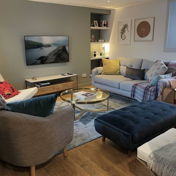 Una sala de estar moderna con sofá, reposapiés, mesa de centro y un televisor de pantalla plana montado en la pared.