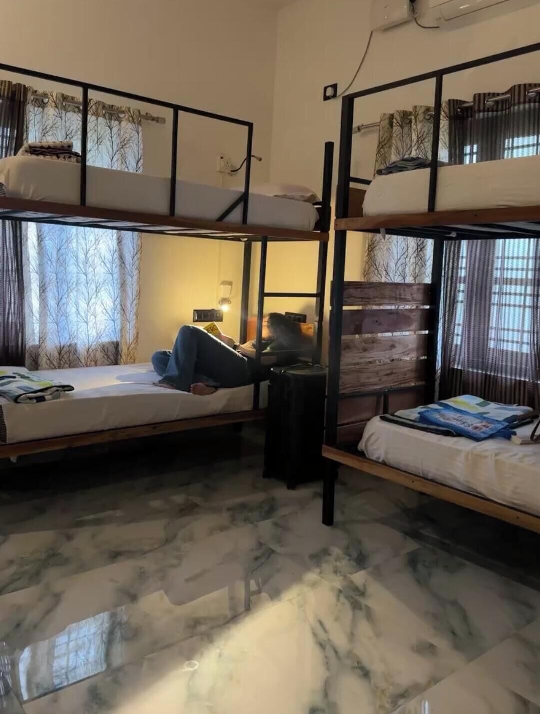 A dormitory room with bunk beds, a small table, and a window with curtains.
