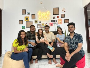 A group of people sitting on a couch in a room with a wall decorated with various framed pictures and a neon sign that reads 'Beach or Beach.' - Beach Oh Beach (Varkala)