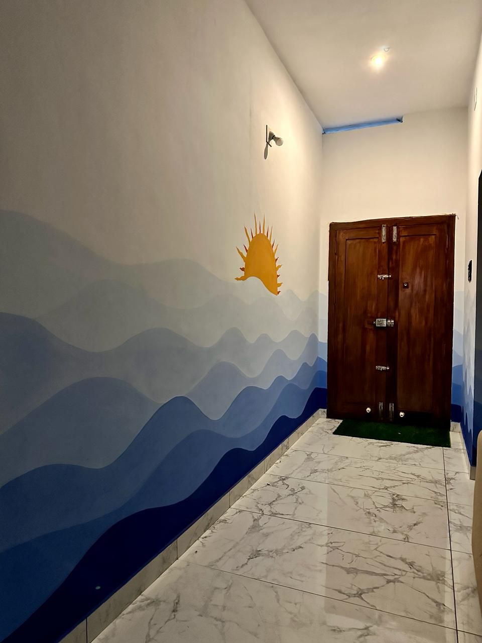 Un pasillo con piso de mármol, un mural en la pared que muestra un sol y montañas, y una puerta de madera.