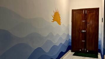 Un pasillo con piso de mármol, un mural en la pared que muestra un sol y montañas, y una puerta de madera.