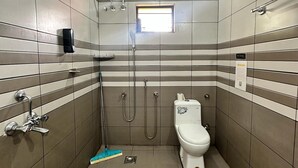 A small, tiled bathroom with a toilet, a shower, and a hand dryer. - Beach Oh Beach (Varkala)