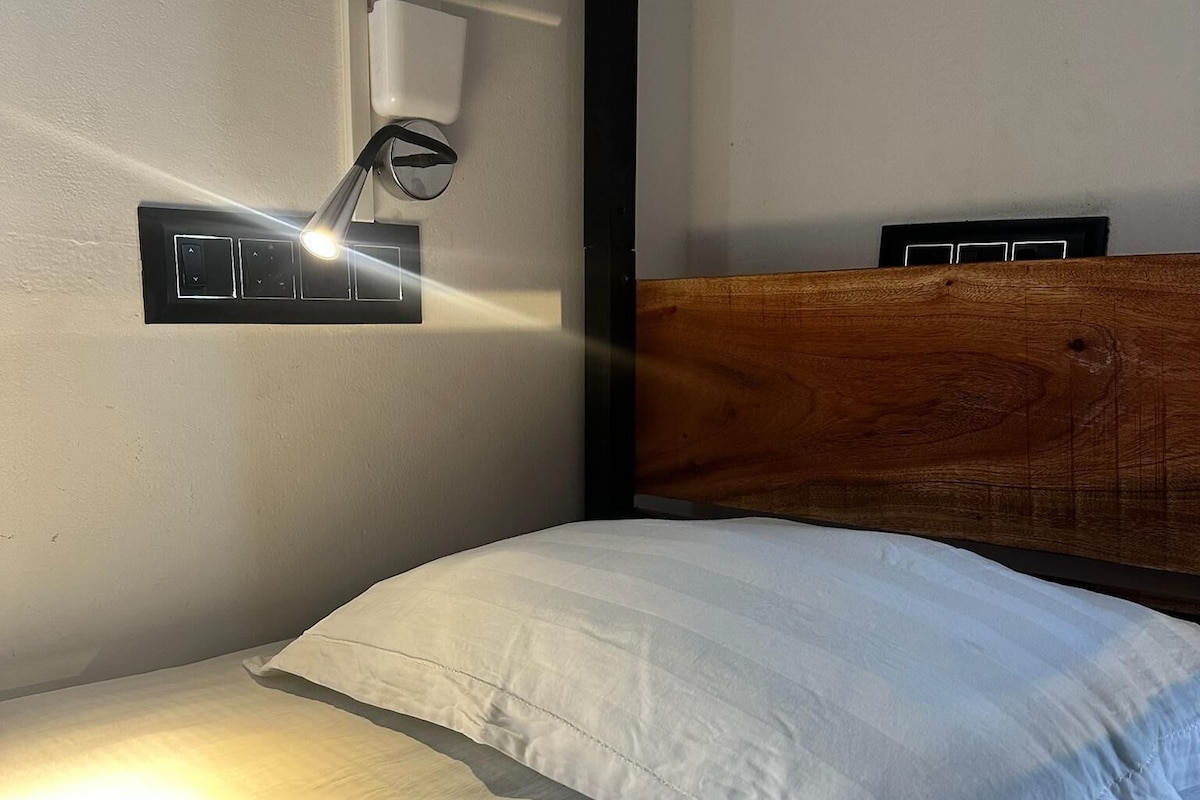 A bed with white bedding, a wooden headboard, and a wall-mounted light fixture.