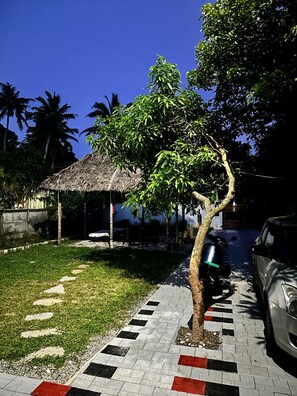 A tree-lined pathway with a thatched-roof structure, a parked car, and a paved area with patterned tiles. - Beach Oh Beach (Varkala)