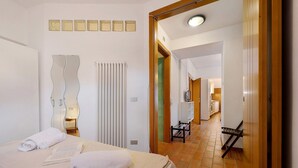 A hotel room with a bed, a mirror, a radiator, and a view into the kitchen area. - Villa G with Lake View, Private Terrace Steps from Lake Garda (Torbole)