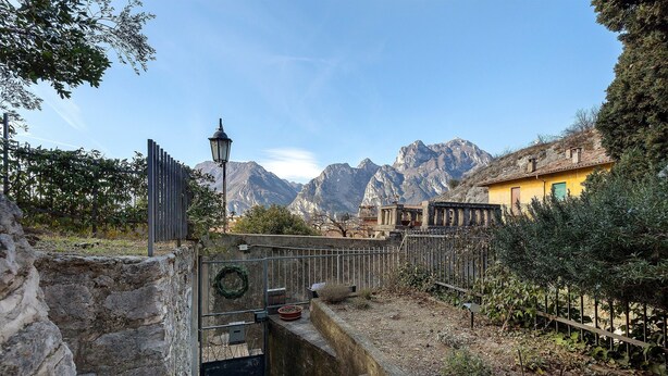 A stone well, a metal gate, a yellow building, and mountains in the background. - Villa G with Lake View, Private Terrace Steps from Lake Garda (Torbole)