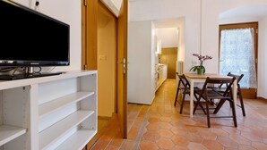 A modern kitchen with white cabinets, a dining table with chairs, and a television on a white shelf. - Villa G with Lake View, Private Terrace Steps from Lake Garda (Torbole)