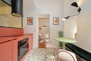 A compact kitchen with a modern stove, a countertop, and a small dining area with a chair and table. - Lussuoso appartamento vicino al Colosseo (Roma)