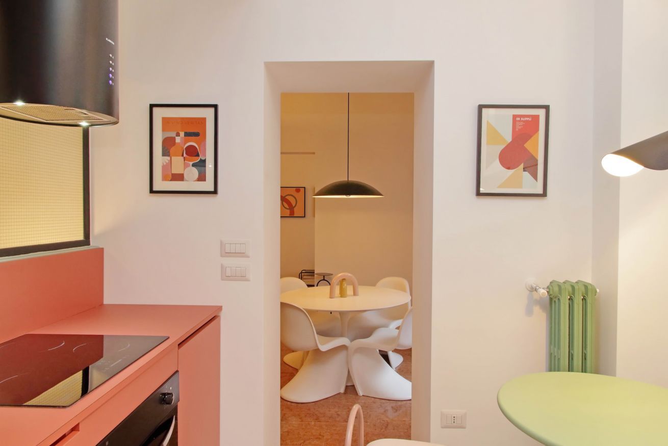 Une cuisine moderne avec un plan de travail rose, une hotte noire et un coin repas comprenant une table ronde et des chaises blanches.