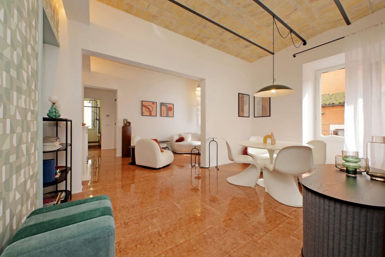 A modern living room with a dining area, a kitchen in the background, and a view of the outside.