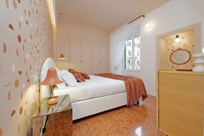 A bedroom with a bed, a nightstand, a lamp, a wardrobe, and a window with curtains. - Lussuoso appartamento vicino al Colosseo (Roma)