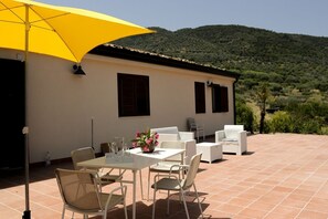An outdoor patio with a table and chairs, a yellow umbrella, and a view of a hilly landscape. - Villa Bruca is a two-family house consisting of two separate units.The proposed unit, Villa Bruca 2, includes a double bedroom with the option of adding one single bed, a spacious bathroom with a modern walk-in shower, and a kitchen-living area equipped  (Caronia)