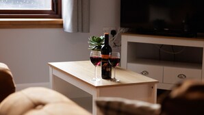 A living room with a sofa, a small table with a bottle and glasses, and a TV on a stand. - NEW to VRBO: Central Lerwick 2Bed Apt · Garden|Walk to Sights (Lerwick)