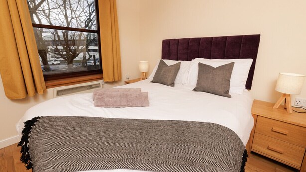 A neatly made bed with a patterned throw, a headboard, and two bedside lamps. - NEW to VRBO: Central Lerwick 2Bed Apt · Garden|Walk to Sights (Lerwick)