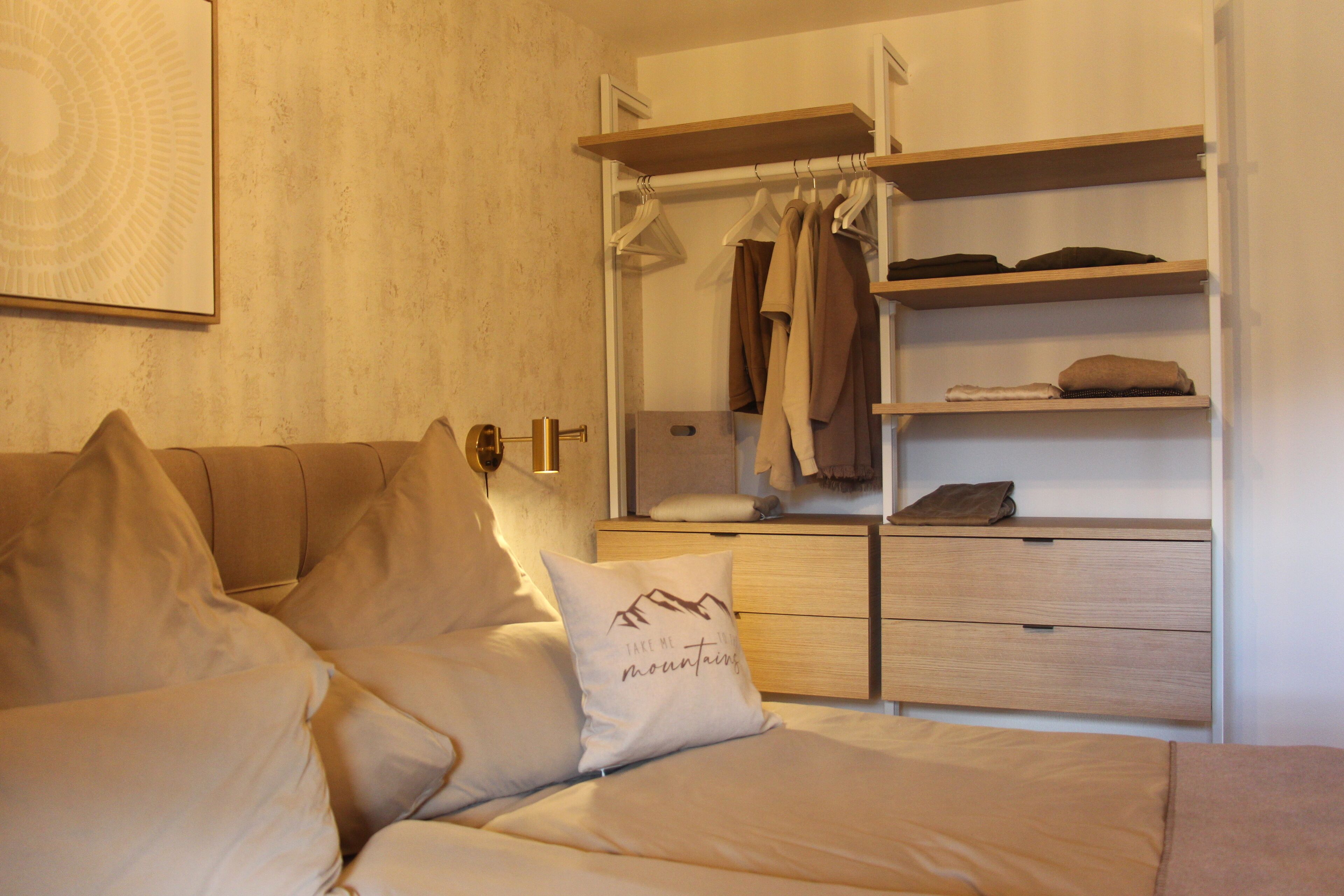 Ein Schlafzimmer mit einem Bett, einem Nachttisch, einem Kleiderschrank und einem an der Wand befestigten Regal.