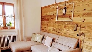 Uma sala de estar moderna com sofá modular, piso de madeira, radiador, janela com cortinas e um quadro pendurado na parede.