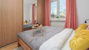 Ett sovrum med en säng, ett sängbord med en lampa, ett fönster med gardiner och utsikt över stadsbilden.