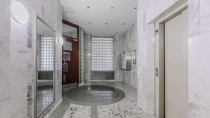 En modern hotellobby med marmorgolv, en central, cirkelformad design och en glasdörr som leder in till ett rum.