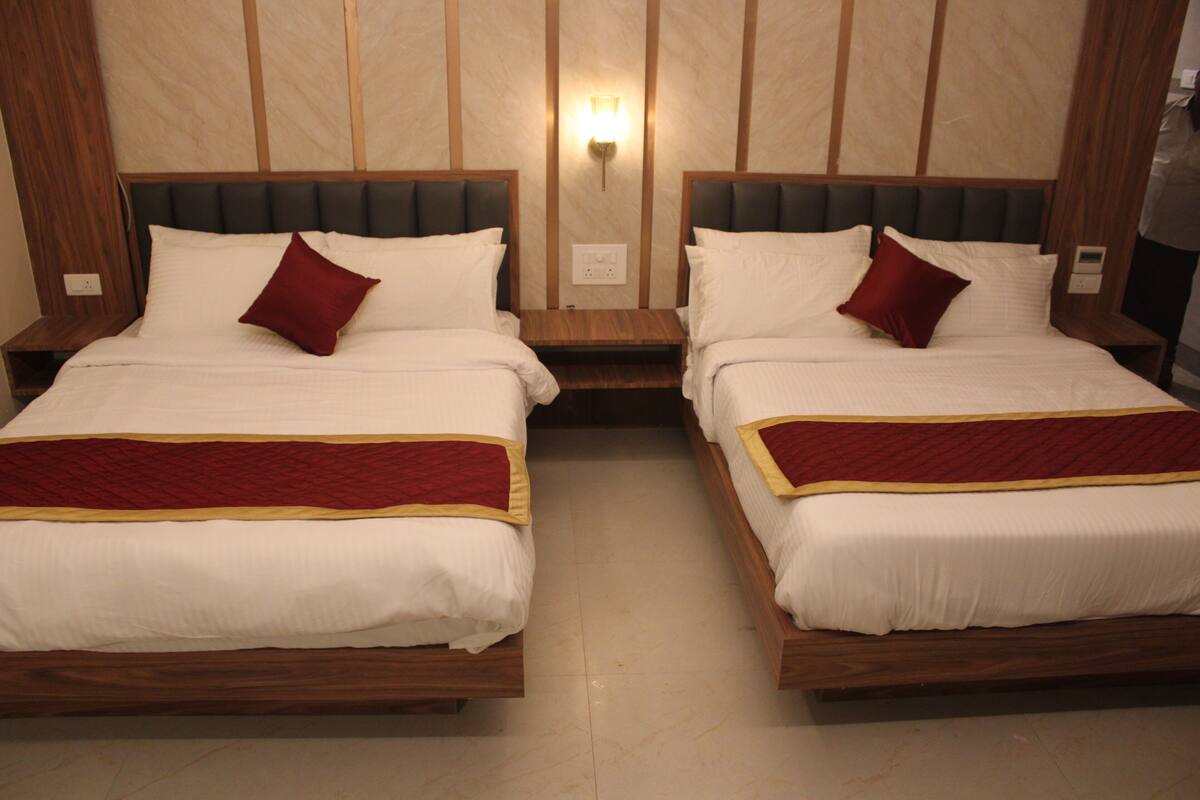 Een hotelkamer met twee bedden, elk voorzien van een houten frame en witte beddengoed. Daartussen staat een nachtkastje met een lamp.