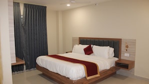 Een net opgemaakt bed met houten frame en wit beddengoed, een nachtkastje met een lamp en een plafondventilator.